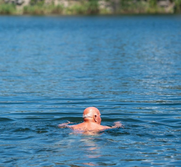 man-swimming-in-a-blue-lake-with-trees-9t9tavlbbj8