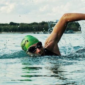 A male swimmer in a green cap and goggles competing in an open water race.